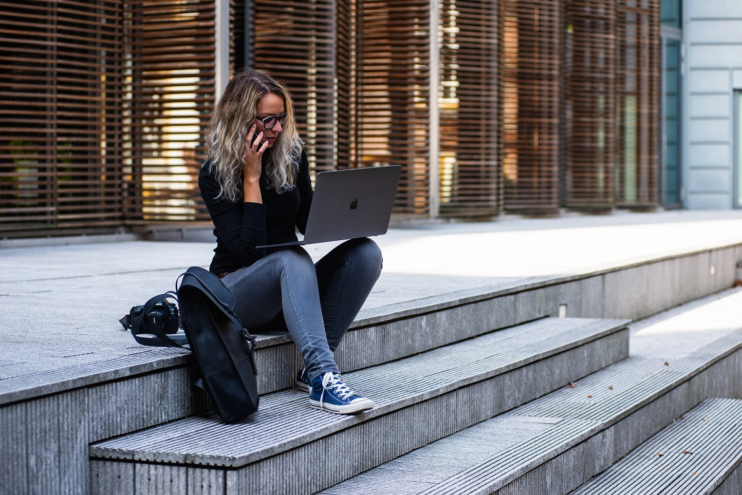 Mulher sentada em uma escadaria com um computador no colo e falando ao celular, demonstrando flexibilidade no trabalho.